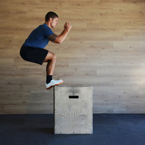 Person jumping onto a pylo box inside a gym. Shop fitness socks.